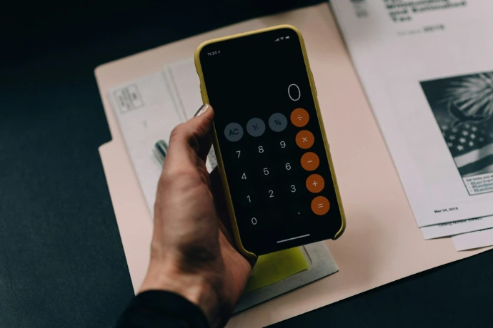 A hand holding a smartphone displaying a calculator app over a paper folder